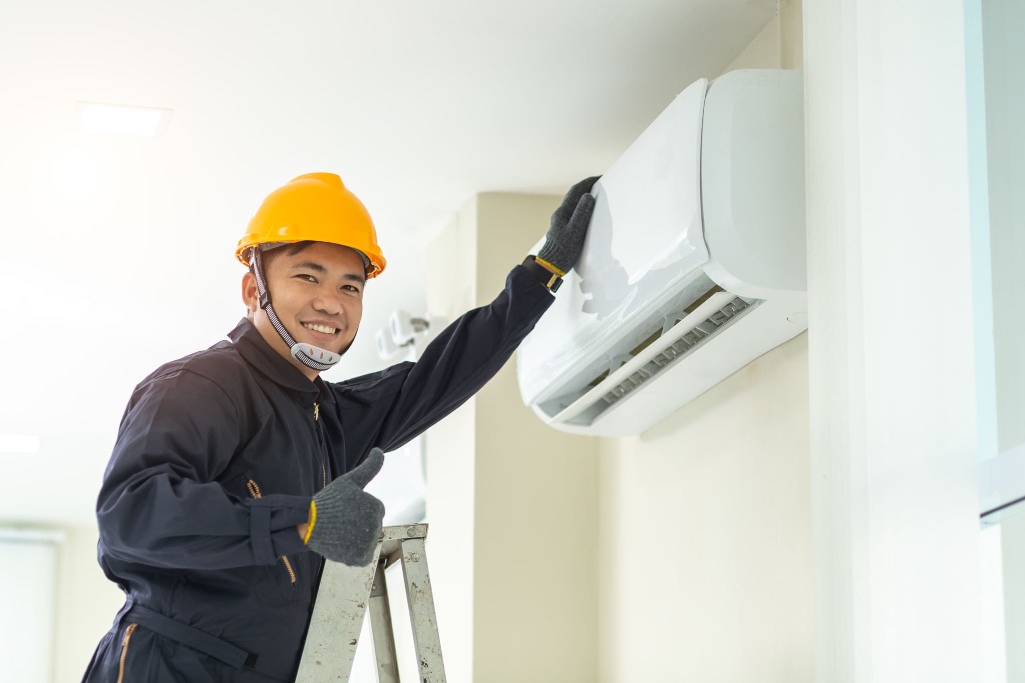 Asian Male technician repairing air conditioner safety uniform indoors.